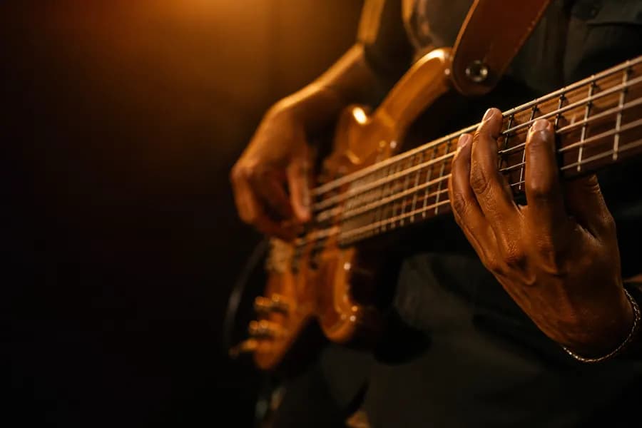 Hands playing a bass guitar, fingers on the strings, lit in warm amber