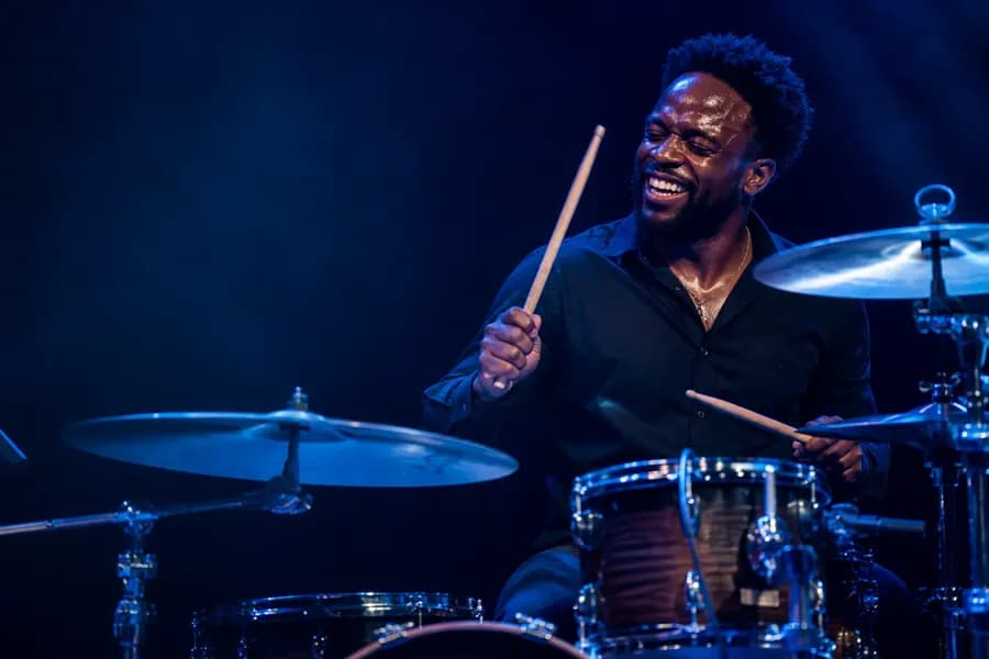 A drummer mid-performance behind a full kit under blue stage lighting