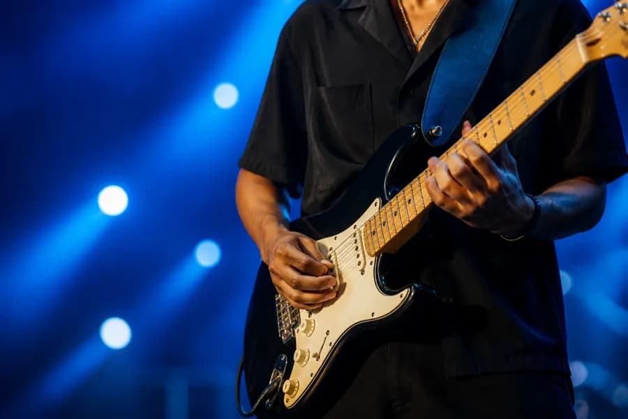 A guitarist playing an electric guitar on stage under blue lighting