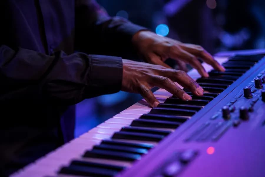 Hands playing an electric keyboard, keys lit in purple and blue
