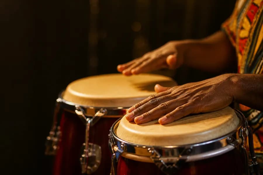 Hands playing a pair of congas, lit in warm golden light