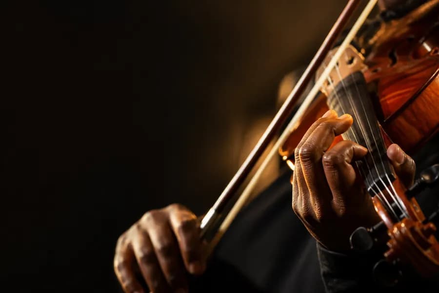 Hands playing a violin, bow drawn across the strings in warm light